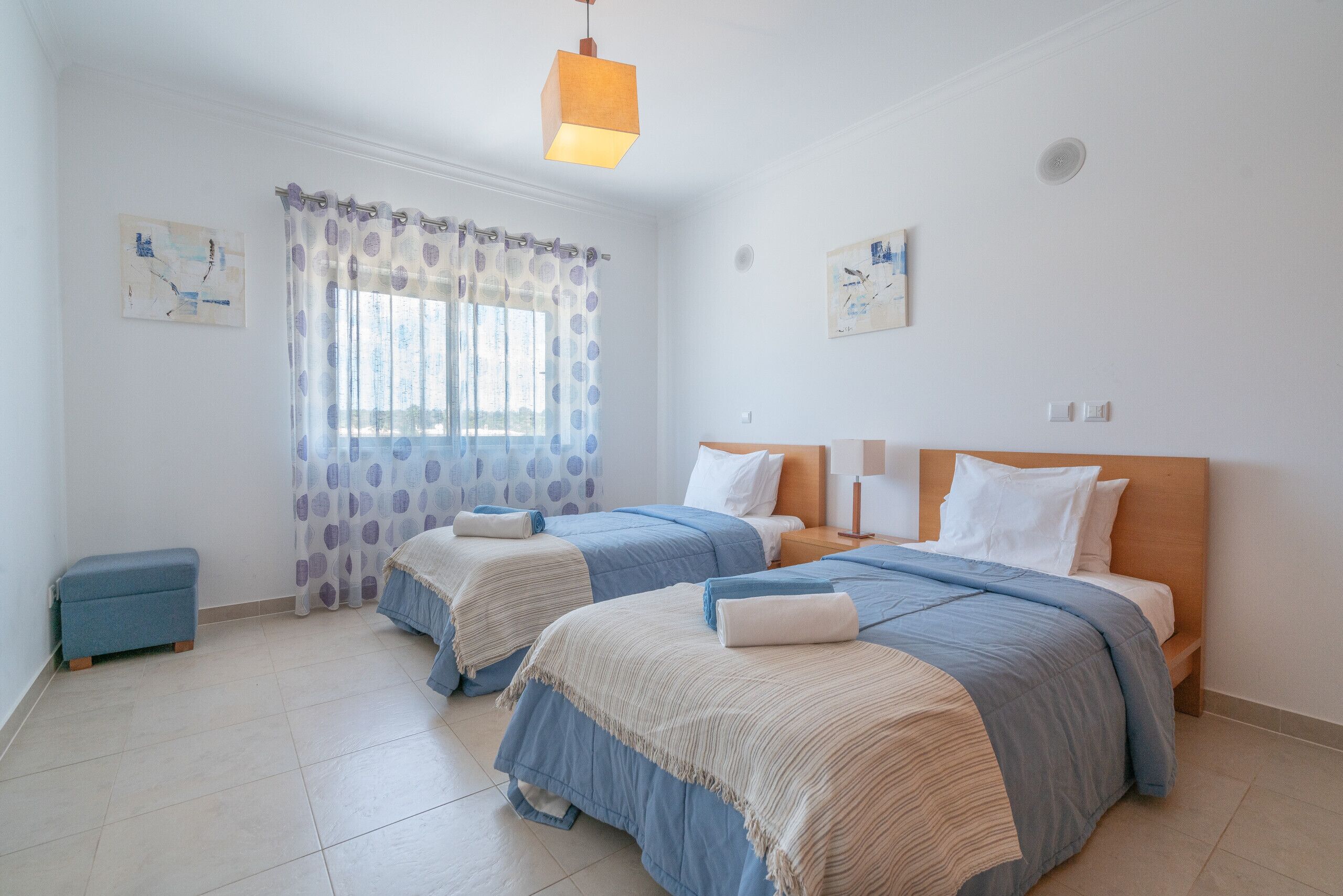Un dormitorio con dos camas, una ventana con cortinas, un banco y obras de arte en las paredes.