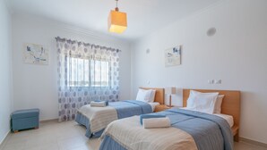 Una camera da letto con due letti, una finestra con tende, una panca e opere d'arte alle pareti.