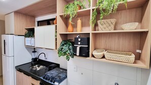 Una cocina con microondas, estufa, pileta y repisas de madera con plantas y cestas.