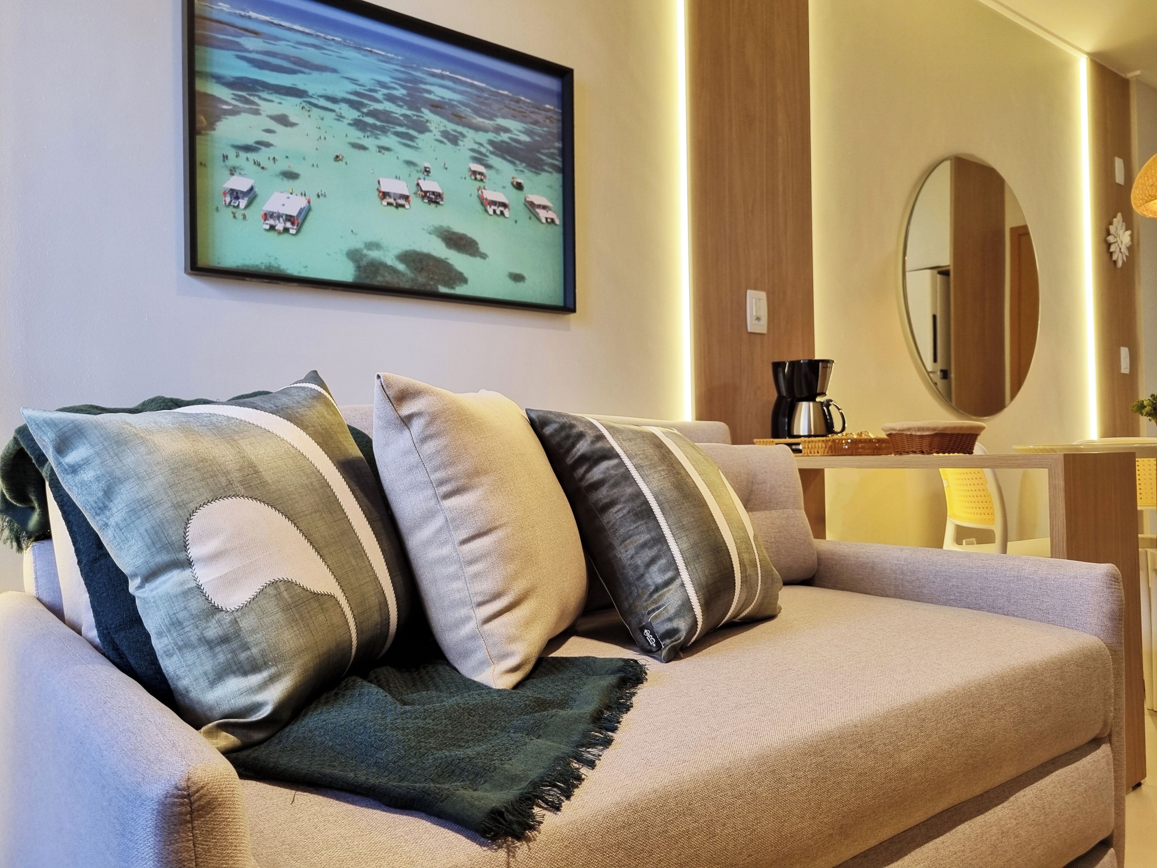 Un salon moderne avec un canapé, une table basse, un miroir et un tableau encadré représentant une scène de plage.