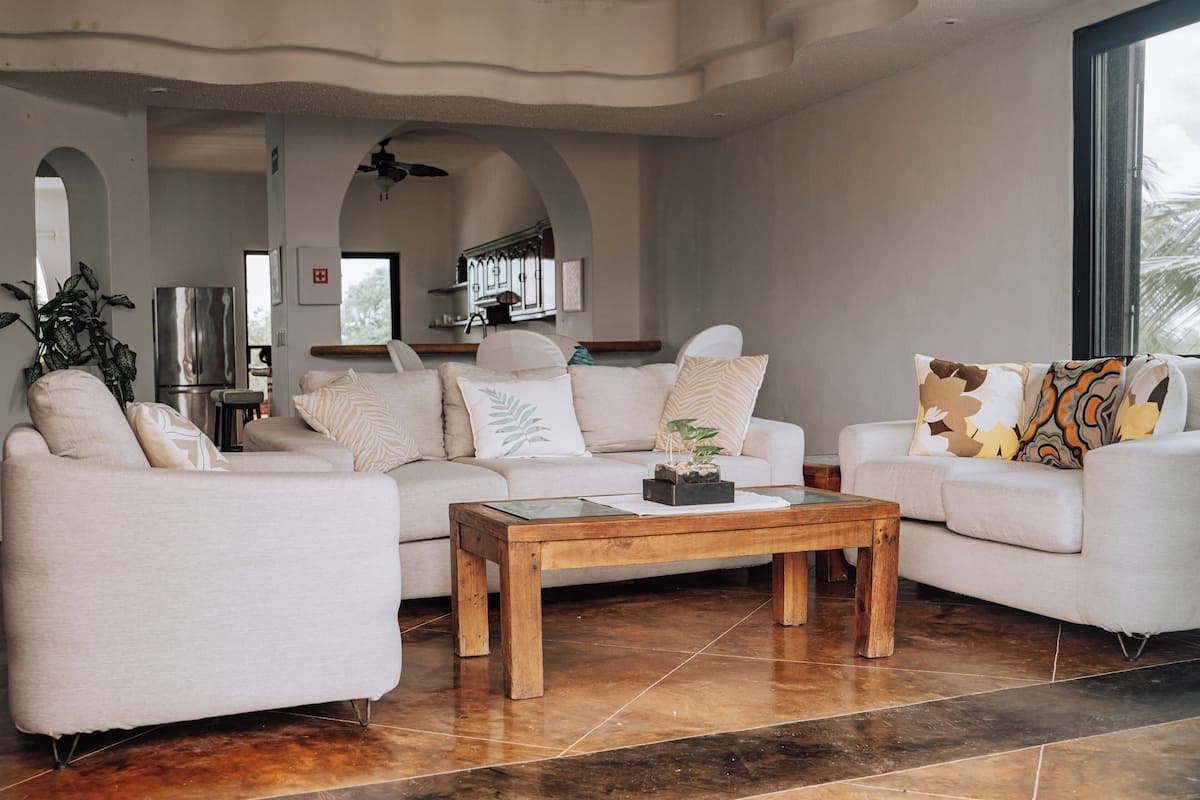 Ein modernes Wohnzimmer mit zwei weißen Sofas, einem Holztisch und einer Küche im Hintergrund.