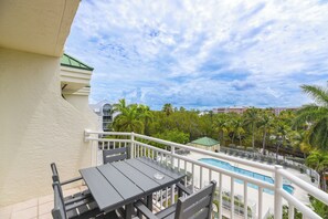 A balcony with a table and chairs, a pool, and palm trees in the background. - The Samana Cay | Tropical, Airy Retreat w/ Private Balcony, Pool! (Key West)