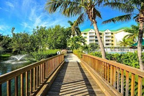 A wooden boardwalk leading to a hotel with a green roof, surrounded by palm trees and a water feature. - The Samana Cay | Tropical, Airy Retreat w/ Private Balcony, Pool! (Key West)