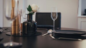 Une table à manger dressée avec une bouteille de vin, un vase de fleurs, un verre, une cuillère et une fourchette.