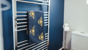 Une serviette ornée d’un motif doré est suspendue à un porte-serviettes en métal dans une salle de bain aux murs bleus.