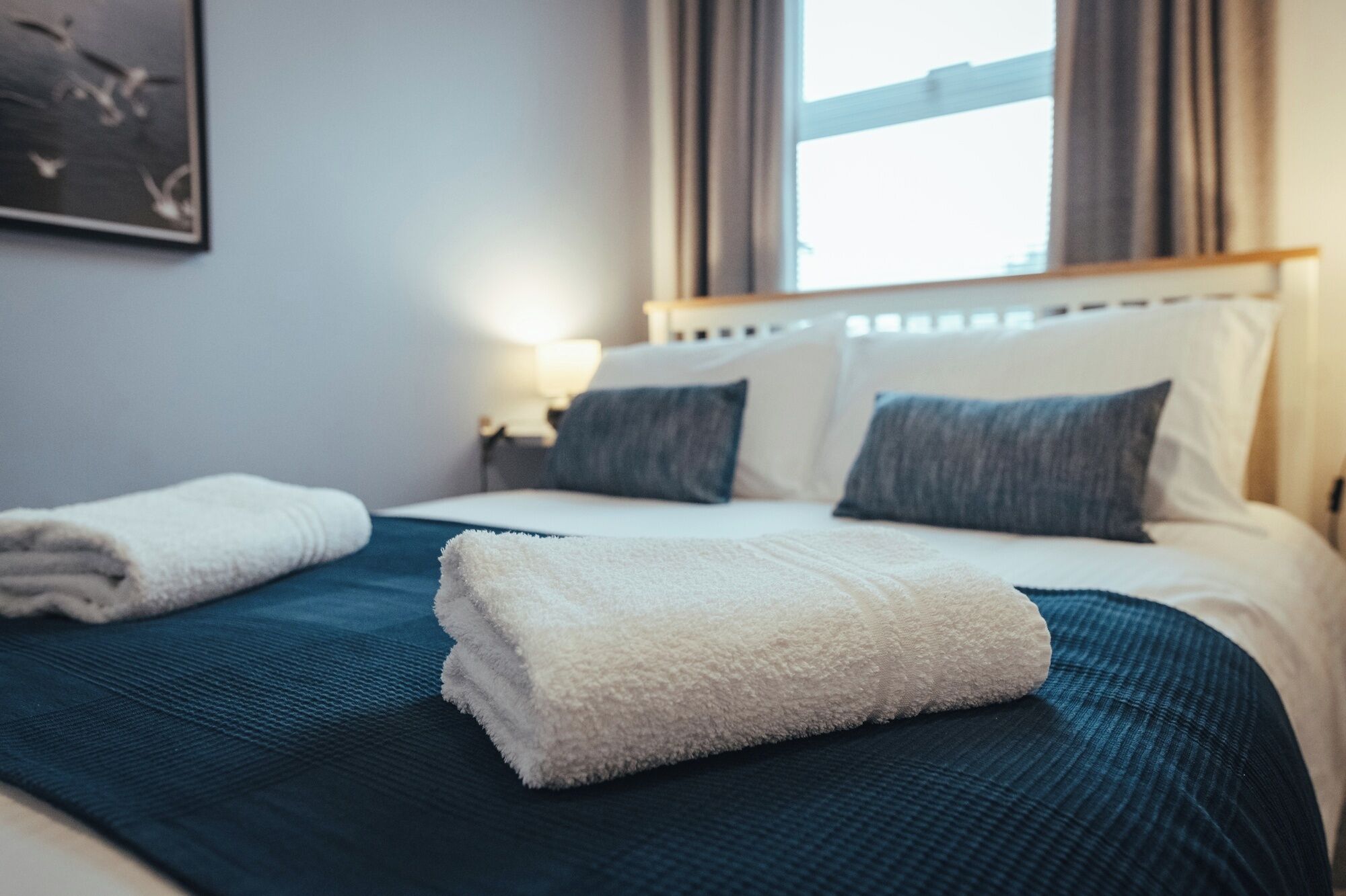 Ein ordentlich gemachtes Bett mit weißer und blauer Bettwäsche, einem Kopfteil und einer Nachttischlampe.