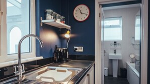 Une cuisine moderne équipée d’un évier en acier inoxydable, d’une bouilloire et d’une horloge murale.
