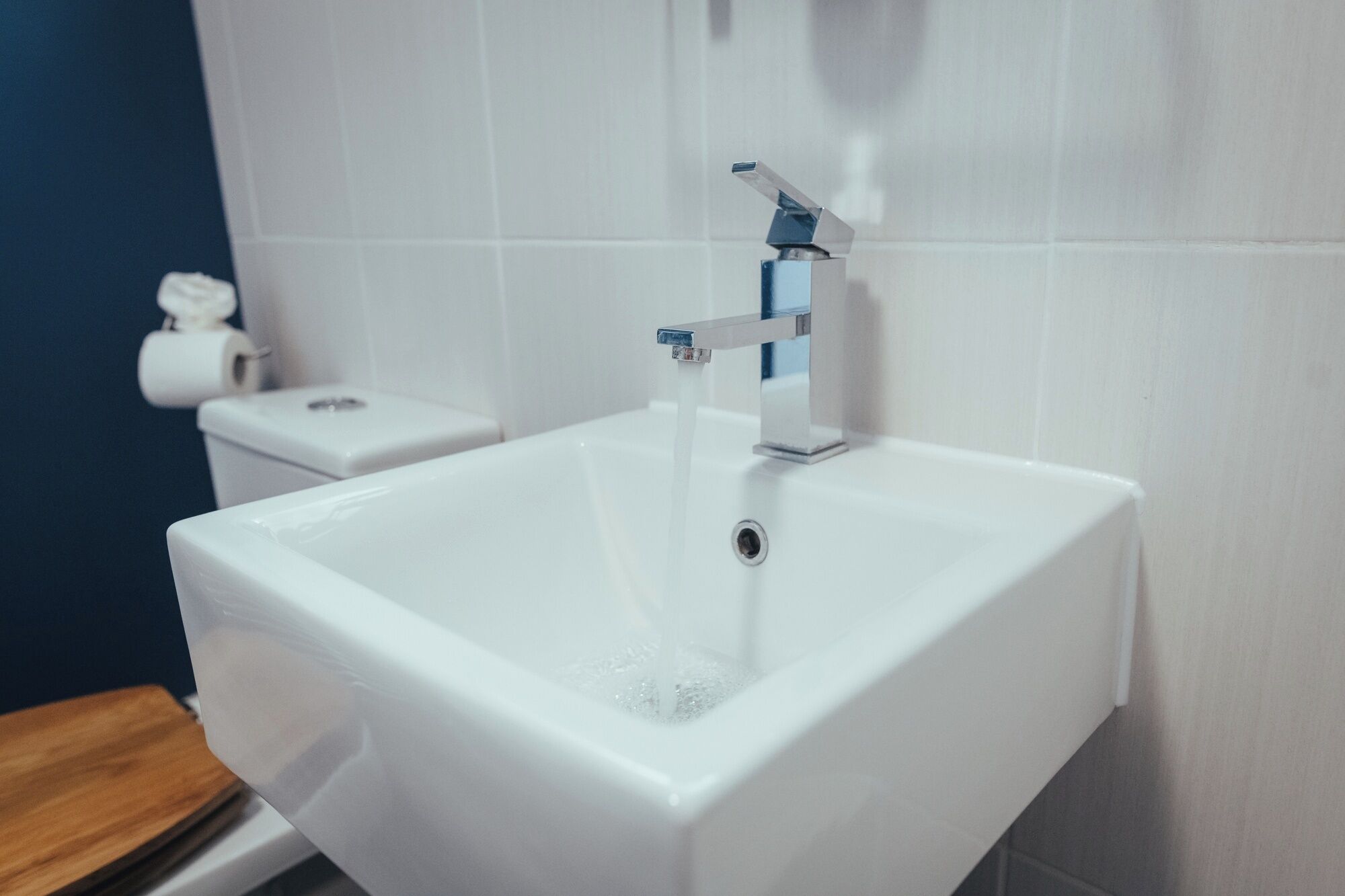 A white bathroom sink with a modern faucet, a toilet, and a roll of toilet paper on the wall.