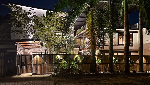 Un bâtiment moderne doté d’un espace extérieur couvert, d’une clôture en bois et de palmiers.