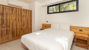 Une chambre avec un grand lit, une tête de lit en bois, des tables de chevet et une fenêtre donnant sur des palmiers.