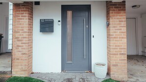A modern building entrance with a grey door, a mailbox labeled "10 Gimli Watch," and a small white planter. - Contractors Retreat- Free Parking (Chelmsford)