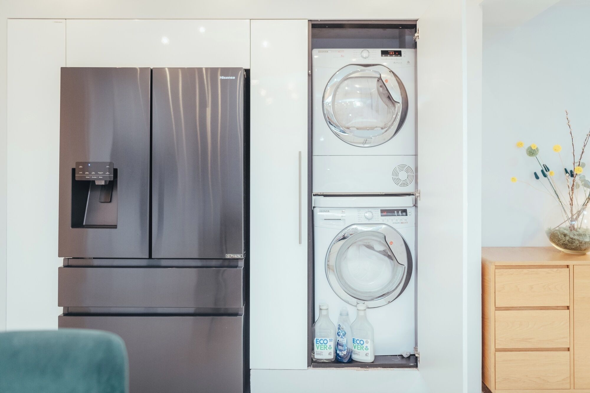 A compact kitchen with a stainless steel refrigerator, a built-in washer and dryer, and a wooden cabinet.