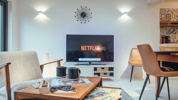 A modern living room with a flat-screen TV displaying 'NETFLIX', a wooden coffee table with magazines, a lamp, and a chair. - Contractors Retreat- Free Parking (Chelmsford)