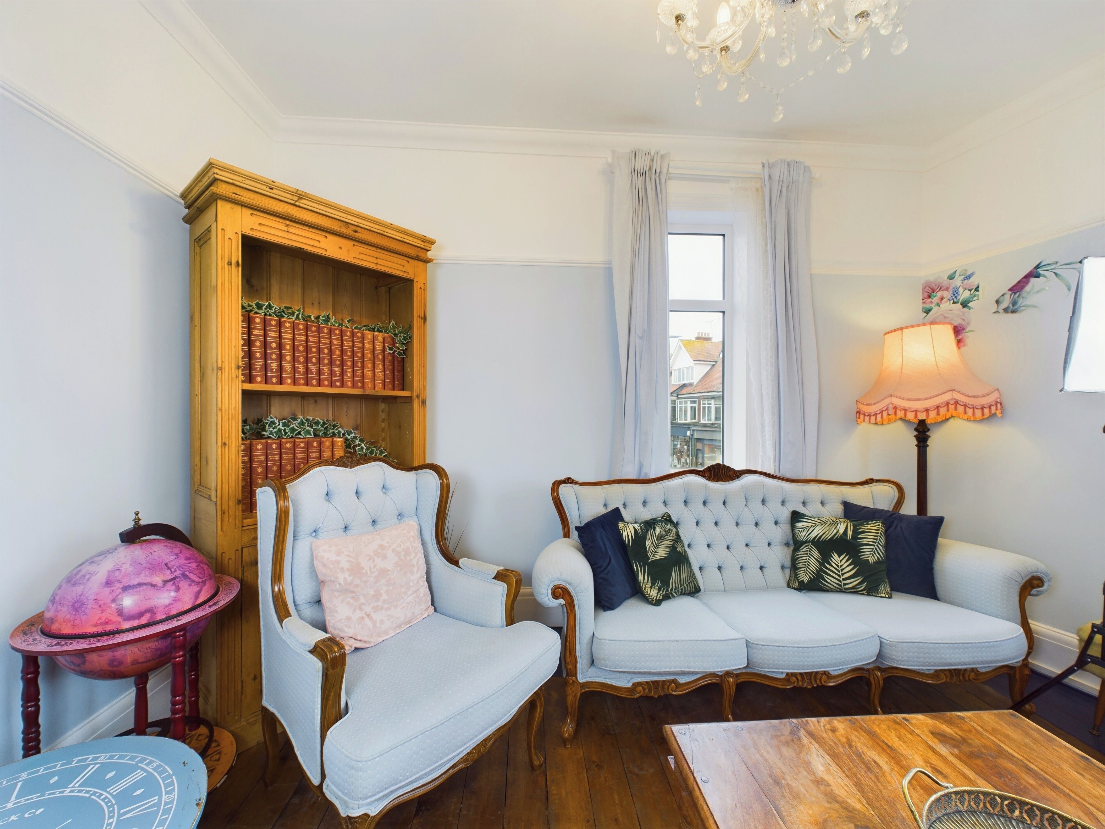 Una sala de estar acogedora con una clásica estantería de madera, un sofá capitonado con cojines estampados, una mesa de centro de madera y una lámpara decorativa.