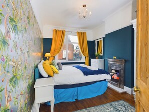 A bedroom with a bed, a dresser, a mirror, a fireplace, and a window with curtains. - Unique 2 bed Leigh-on-sea- With Real Piano (Leigh-on-Sea)