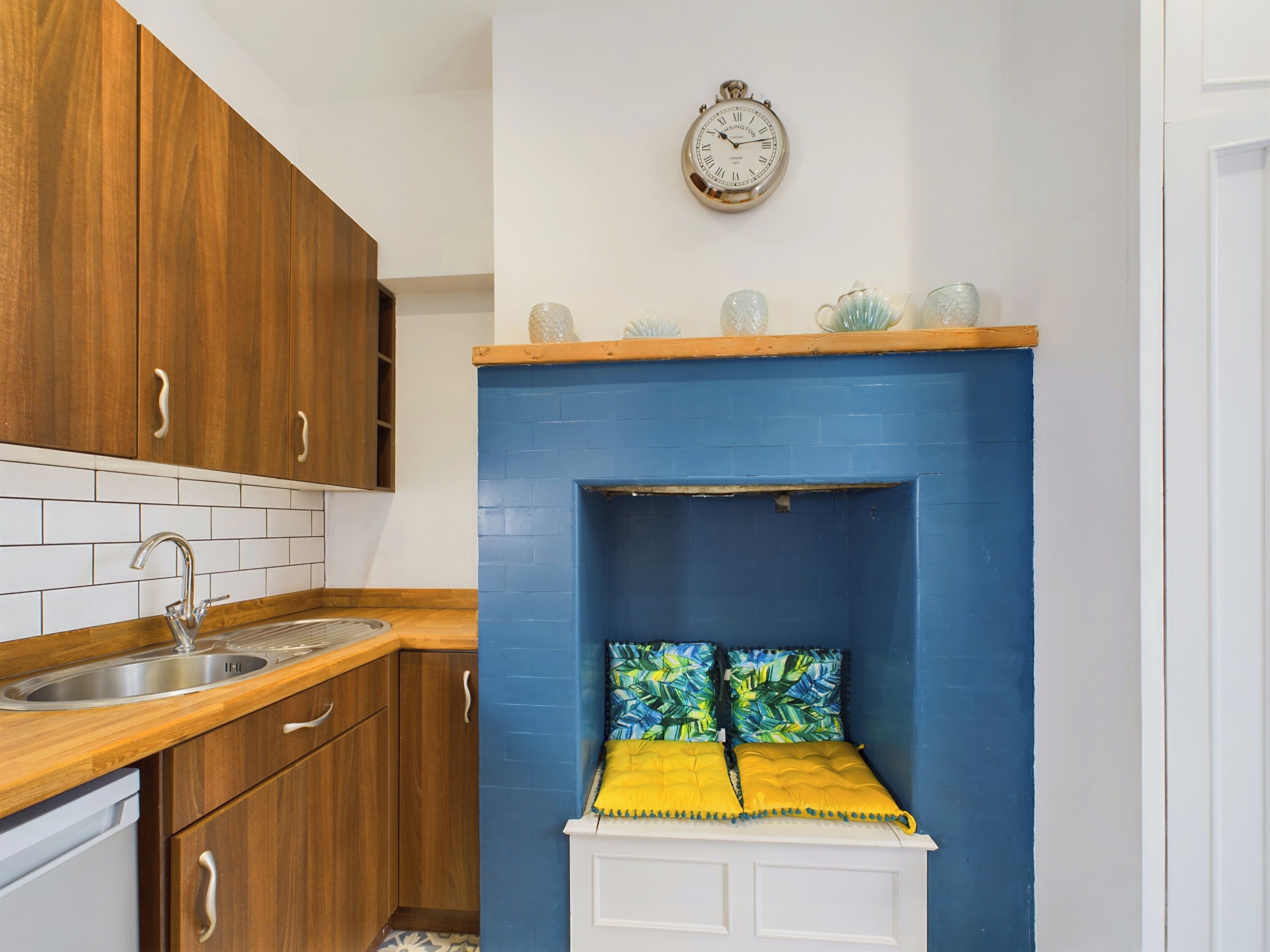 Une cuisine avec des meubles en bois, un évier en acier inoxydable, un mur d’accent bleu, une horloge et des vases décoratifs en verre.
