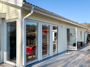 A house with large sliding glass doors, a wooden deck, and a red chair visible through the doors. - 4 Star Holiday Home in Stenungsund (Stenungsund)