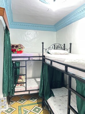A dormitory room with bunk beds, a green curtain, and patterned floor tiles. - aline hostel (Chefchaouen)