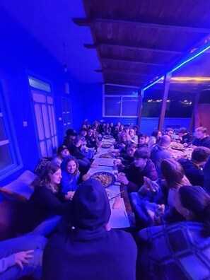 A group of people seated around a long table in a room with blue lighting, large windows, and a wooden ceiling. - aline hostel (Chefchaouen)