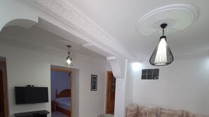A spacious living room with a marble floor, a television on a stand, a sofa, and a coffee table. - aline hostel (Chefchaouen)