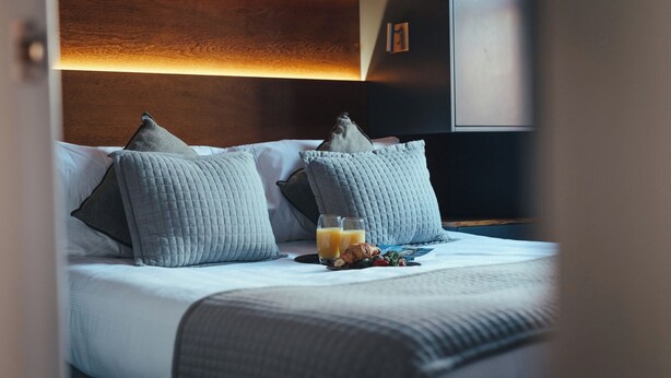 A neatly made bed with two pillows, a tray with croissants and juice, and a wooden headboard. - London Luxury Apartment on Rupert Street (London)