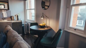 A cozy living area with a sofa, a dining table with chairs, a coffee machine, and a view of the outside through a window. - London Luxury Apartment on Rupert Street (London)