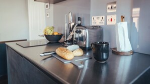 A kitchen counter with a toaster, a bowl of fruit, a cutting board with bread, a black mug, and a white napkin holder. - London Luxury Apartment on Rupert Street (London)
