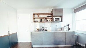 A modern kitchen with a central island, wooden shelves above the sink, and a microwave. - London Luxury Apartment on Rupert Street (London)