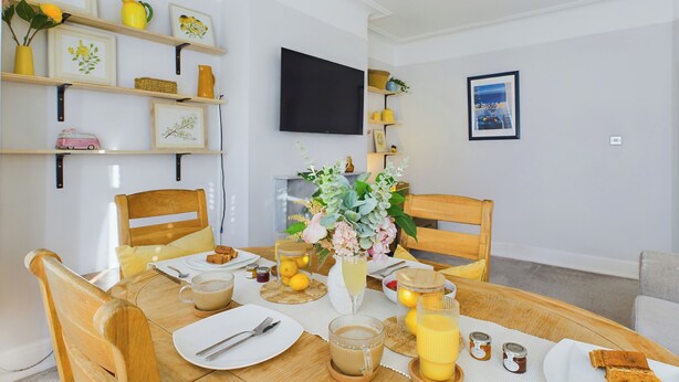A dining area with a wooden table set for breakfast, including plates, cups, and a vase with flowers. - Seaside Haven Retreat in Southend (Southend-on-Sea)