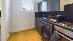 A compact kitchen with a washing machine, a stove, and a window. - Seaside Haven Retreat in Southend (Southend-on-Sea)
