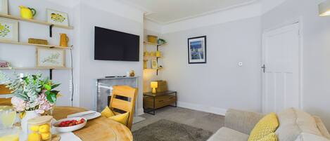 A living room with a sofa, a dining table with breakfast items, a television, and a fireplace.