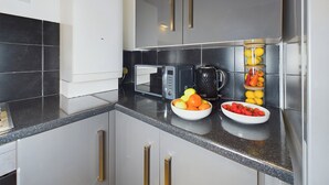 A modern kitchen with grey cabinets, a white refrigerator, a microwave, and two bowls of fruit on the counter. - Seaside Haven Retreat in Southend (Southend-on-Sea)