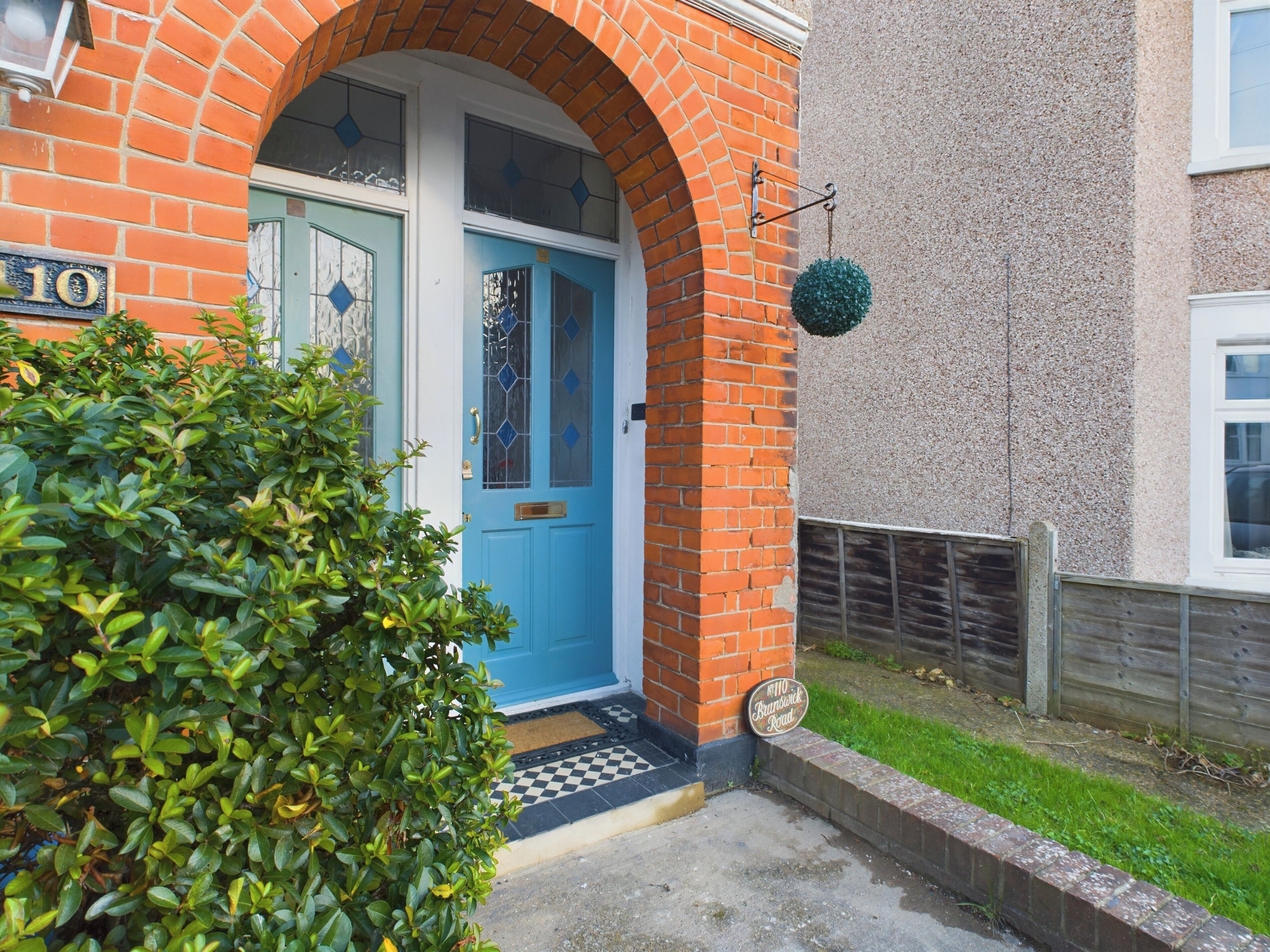 A blue door with a glass panel, a brick archway, and a small green bush in front.
