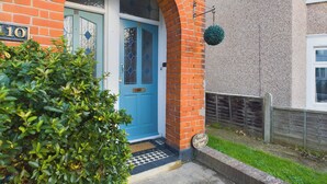 A blue door with a glass panel, a brick archway, and a small green bush in front. - Seaside Haven Retreat in Southend (Southend-on-Sea)