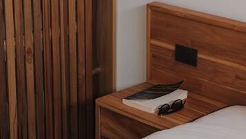 A wooden bed with a white mattress, a wooden nightstand with a book and glasses, and a wooden wardrobe.