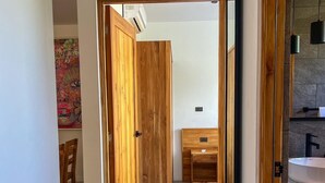 Ein Flur, der zu einem Badezimmer mit Holztür, Waschbecken und Spiegel führt.
