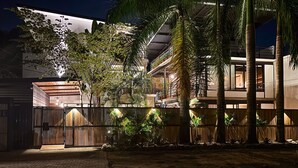 Un edificio moderno con un espacio al aire libre techado, cerca de madera y palmeras.