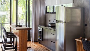 A modern kitchen with stainless steel appliances, wooden flooring, and large windows offering a view of greenery.