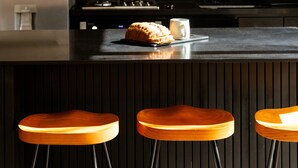 Una cocina moderna con un salpicadero de ladrillo negro, un refrigerador de acero inoxidable, una encimera de madera y dos lámparas colgantes de mimbre.