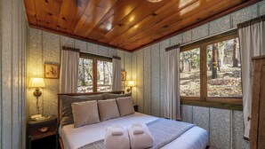 A bedroom with a large bed, two bedside lamps, a nightstand, and a view of the outdoors through a window.