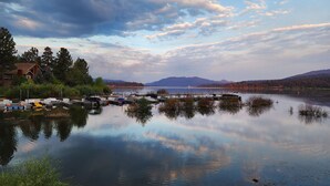 A calm lake with docked boats, a house on the left, and mountains in the background.