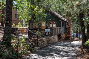 Une cabane rustique avec des fondations en pierre, une terrasse en bois et un escalier menant à l’entrée.