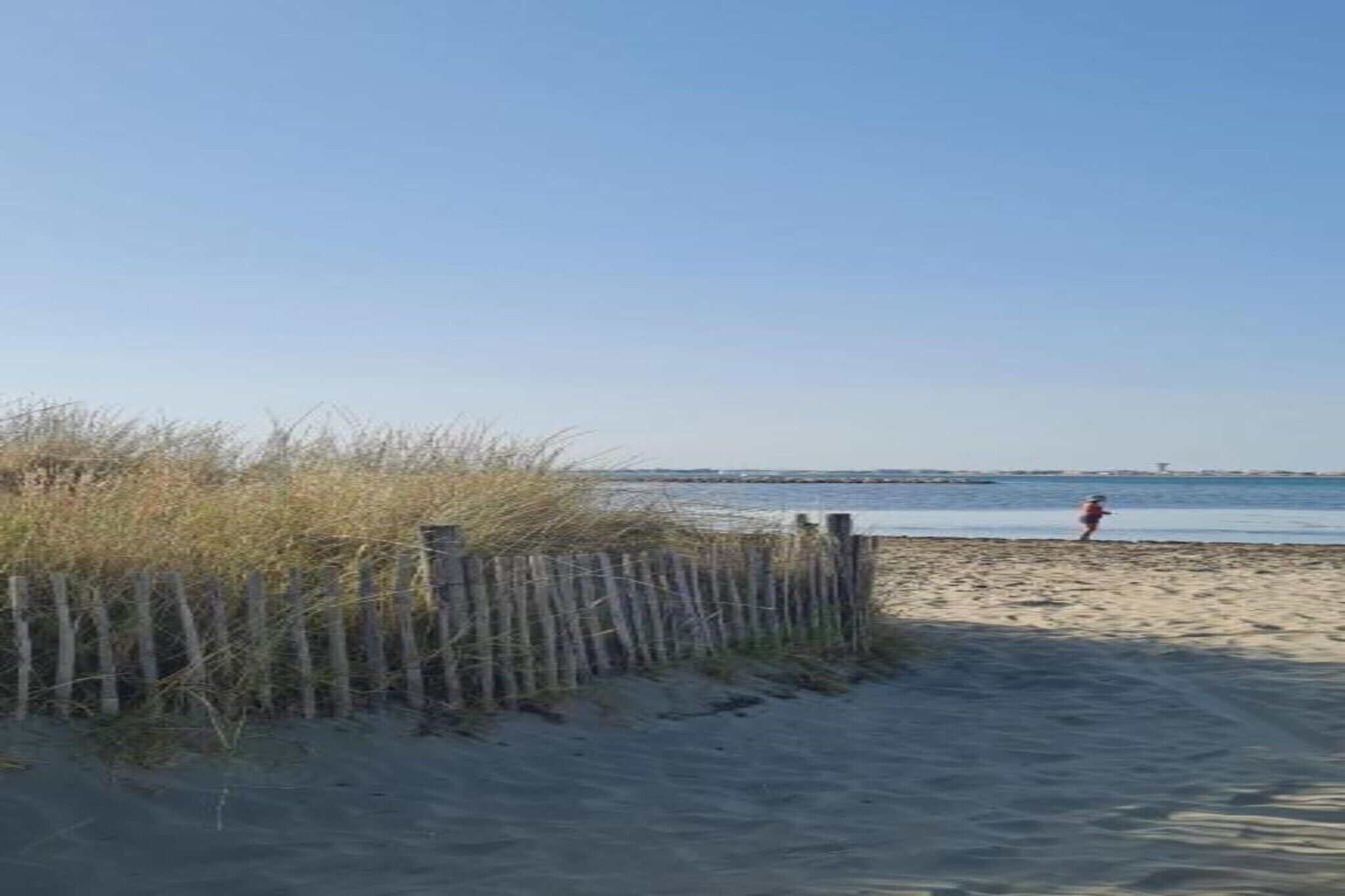 Une plage de sable avec une clôture en bois et une personne au loin.