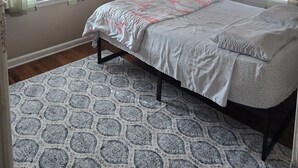 Ein Schlafzimmer mit einem Bett, einem gemusterten Teppich und zwei mit Vorhängen versehenen Fenstern.