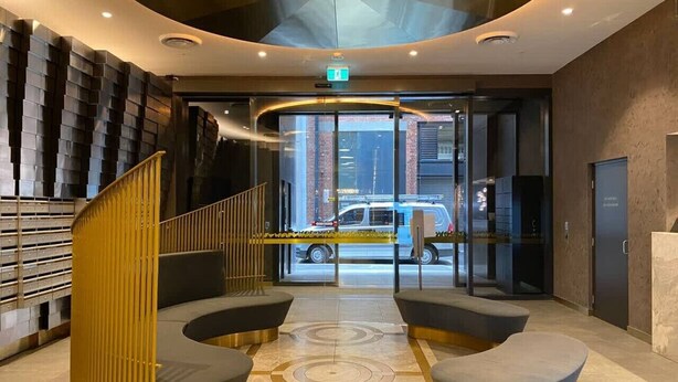 A modern lobby with a curved staircase, seating area, and a glass door leading outside. - Luxury Apt in Rundle Mall with Beautiful City View (Adelaide)
