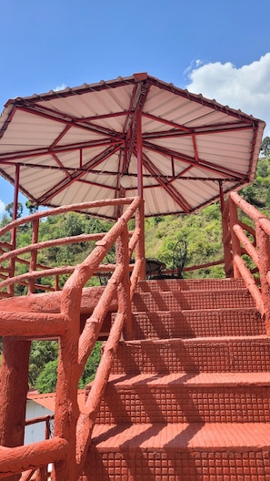 A red-brick structure with a large umbrella-like roof, surrounded by greenery. - Ceyone Classic Fall Resort (Mussoorie)