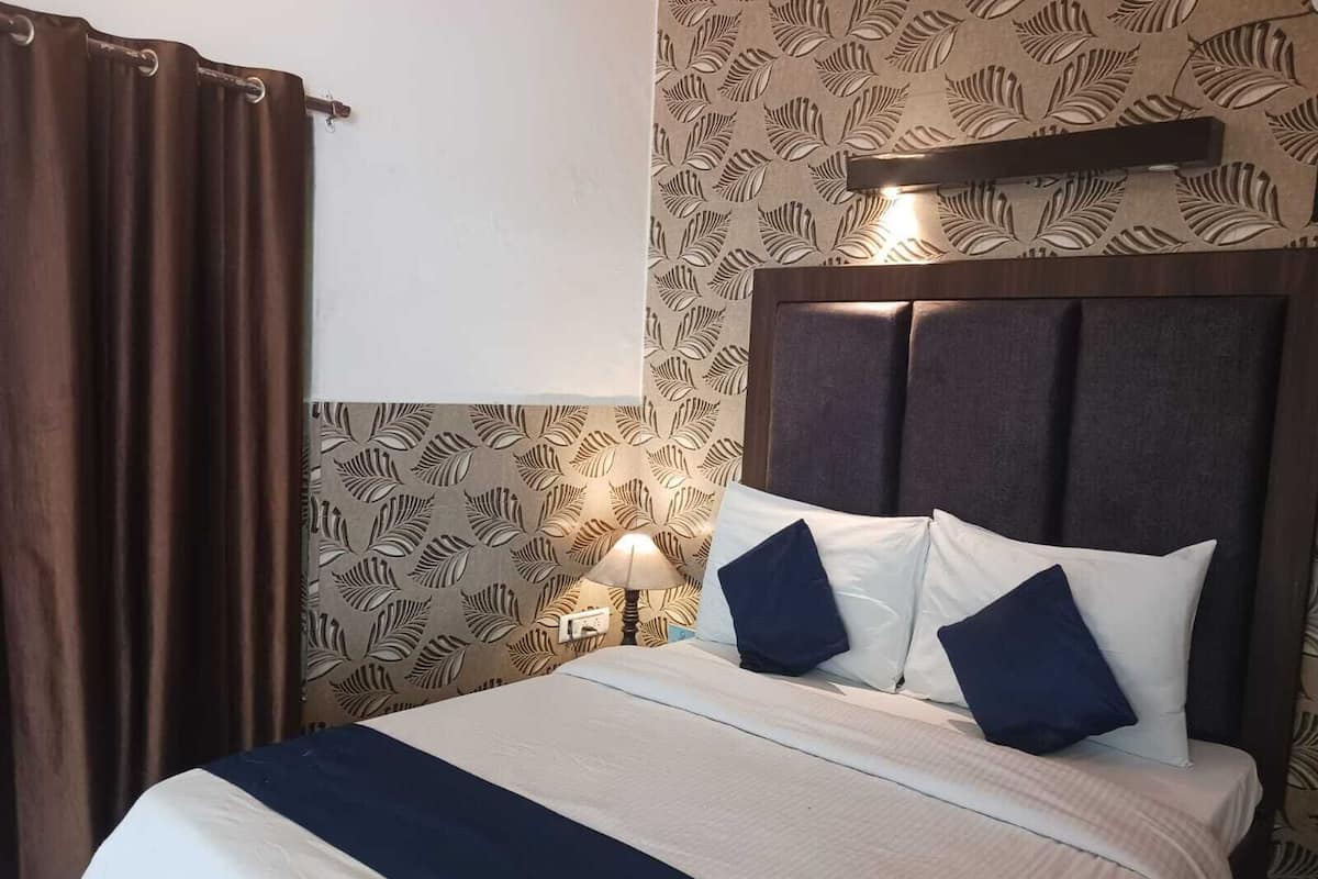 A hotel room with a bed, a nightstand, a lamp, and a wall with a leaf pattern.
