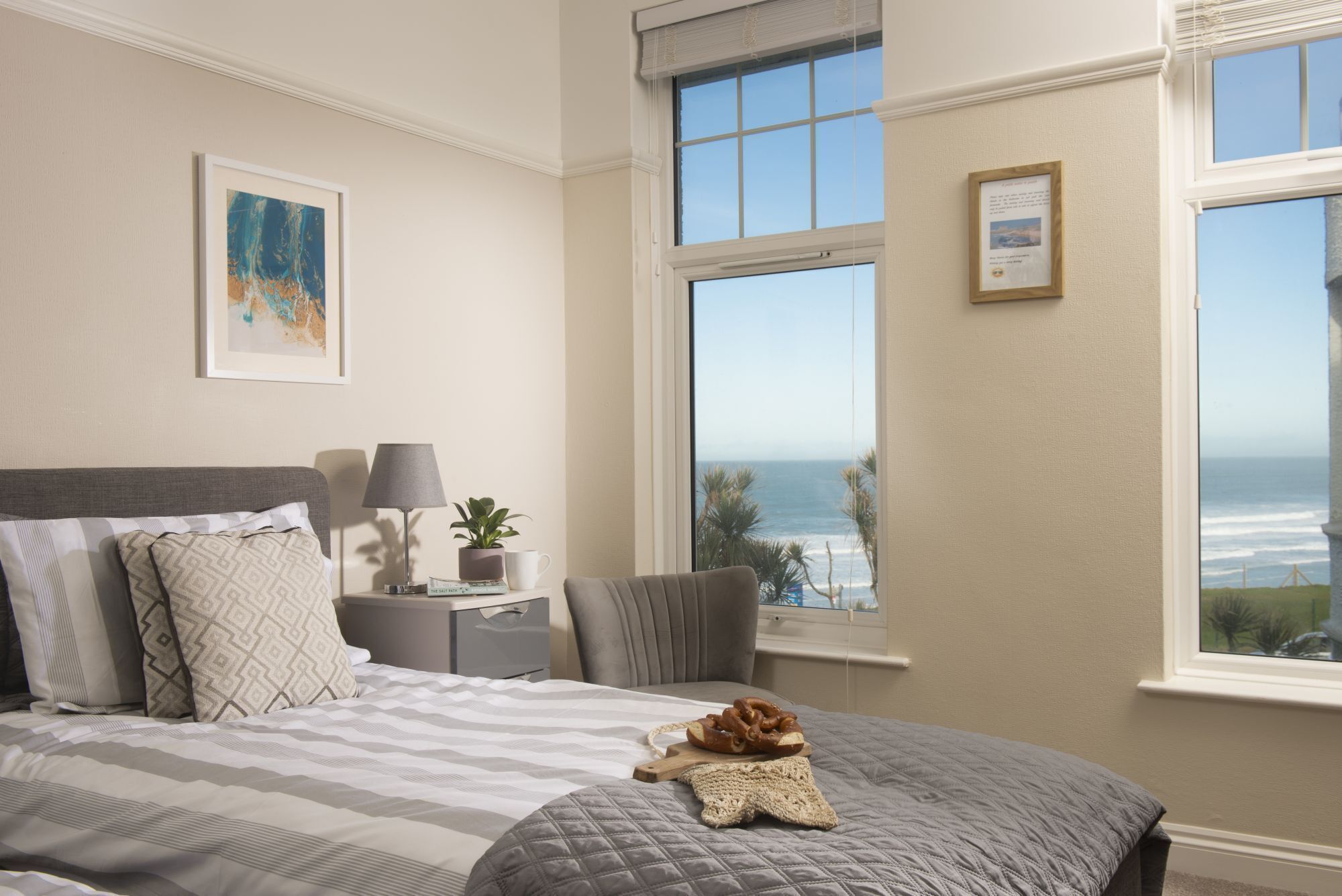 A bedroom with a large bed, a nightstand, a lamp, a framed picture, and a view of the ocean.