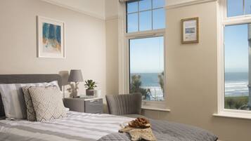 A bedroom with a large bed, a nightstand, a lamp, a framed picture, and a view of the ocean.