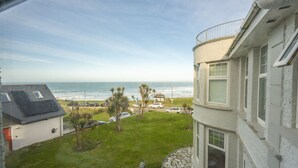 Une vue sur la côte depuis un balcon donnant sur un espace verdoyant où sont garées des voitures, une plage et un ciel dégagé.